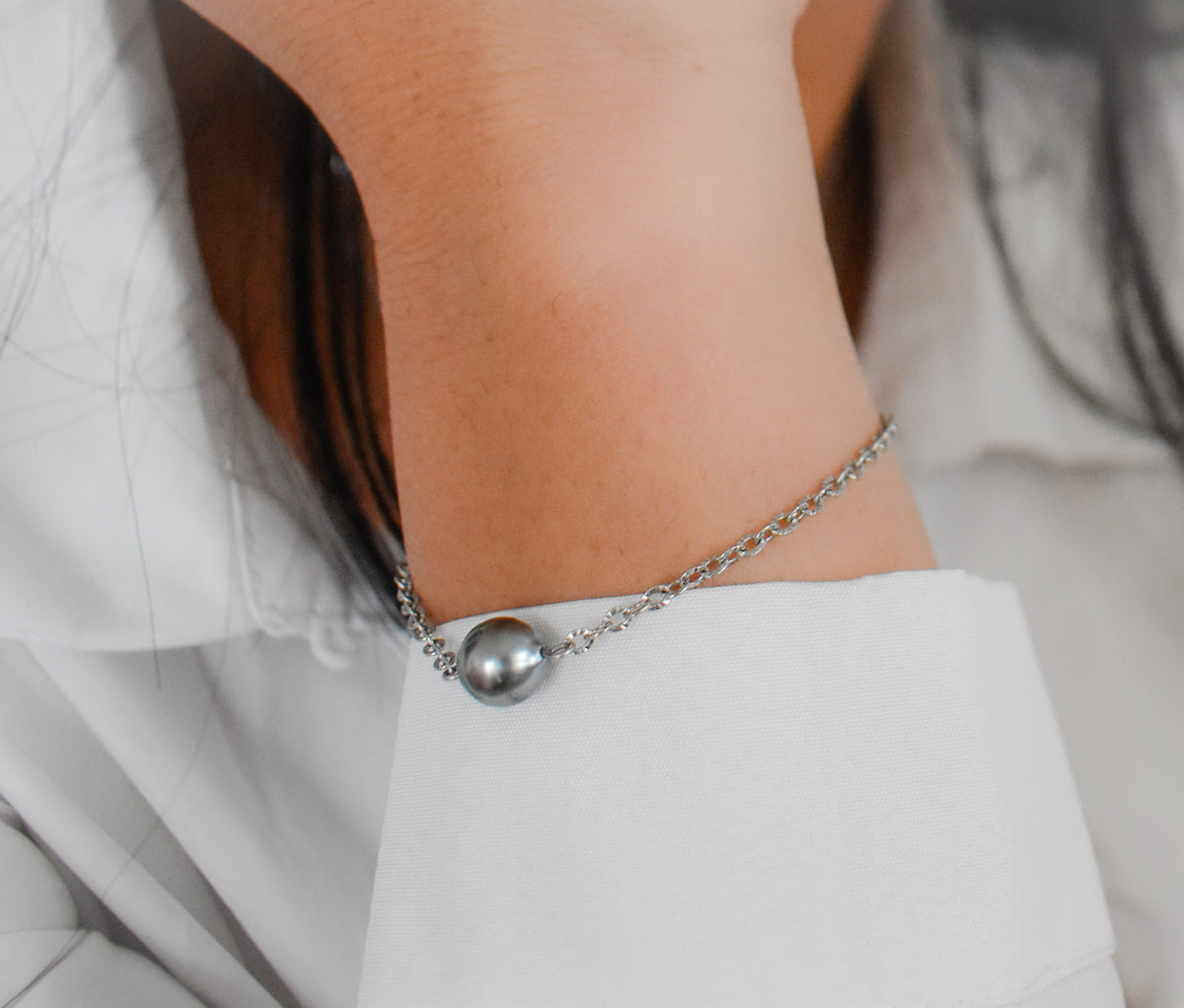 Femme portant à son poignet ce bracelet simpliste en chaîne fine avec à son centre une petite perle de Tahiti. 